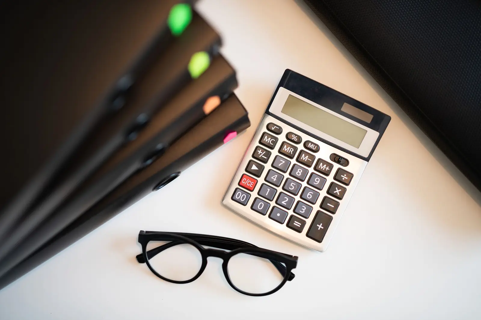 Calculadora, lentes y carpetas sobre un escritorio